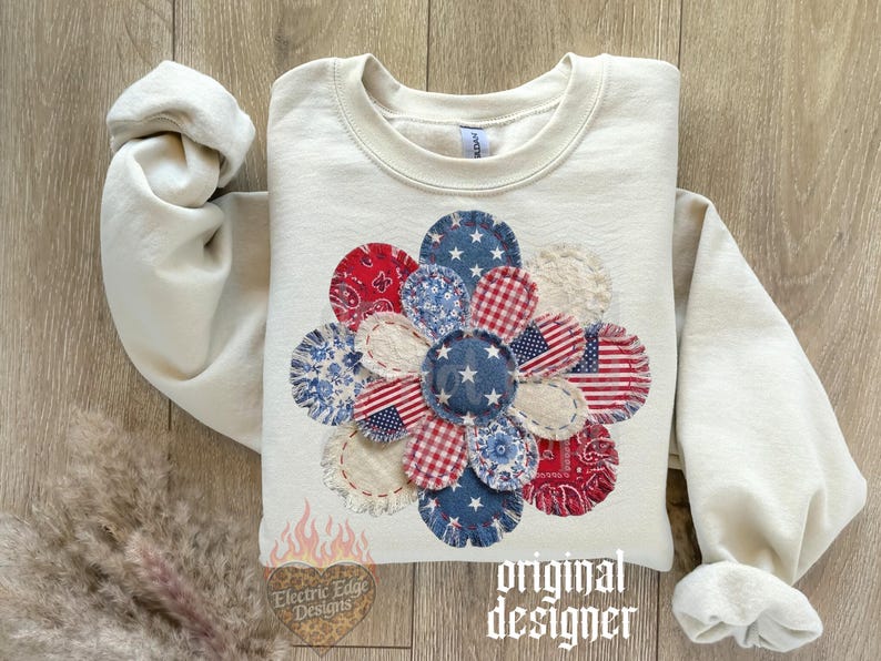 May include: Cream-colored sweatshirt featuring a large, appliqued flower design. The flower is composed of various fabric patches in red, white, and blue patterns, including stars, stripes, and paisley. The text "original designer" is visible.