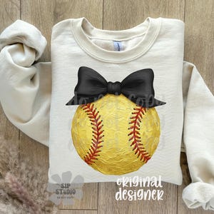 Pu&ograve; includere: Felpa color crema con un grande pallone da softball giallo con cuciture rosse e un fiocco nero. Le parole "original designer" sono stampate in basso a destra. Il testo "SIP STUDIO" &egrave; stampato in basso a sinistra.