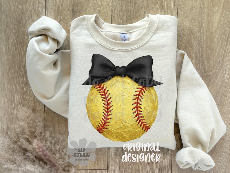 Pu&ograve; includere: Felpa color crema con un grande pallone da softball giallo con cuciture rosse e un fiocco nero. Le parole "original designer" sono stampate in basso a destra. Il testo "SIP STUDIO" &egrave; stampato in basso a sinistra.