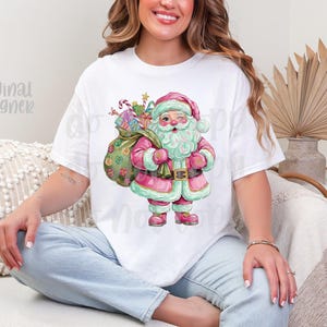 May include: White t-shirt with a watercolour illustration of Santa Claus in pink and green, carrying a sack of gifts. The design includes candy canes and wrapped presents, ideal for the festive season.