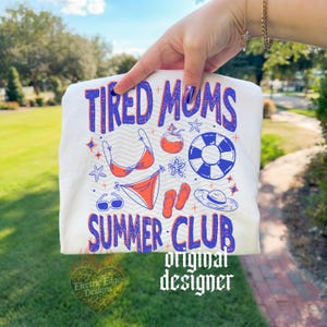 May include: A white t-shirt with the text "TIRED MOMS SUMMER CLUB" in blue and red. The shirt features summer-themed illustrations, including a bikini, sunglasses, and a life preserver. The words "original designer" are also printed on the shirt.