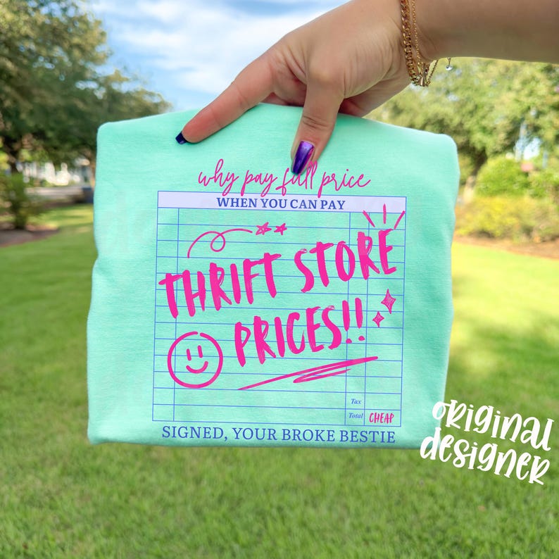 May include: A light green t-shirt with the text "Why pay full price when you can pay Thrift Store Prices!!" in pink. The shirt has a receipt-like design with a smiley face and the words "Signed, Your Broke Bestie."