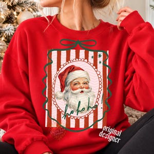 May include: A bright red crewneck sweatshirt featuring a central graphic of a vintage-style Santa Claus face inside a scalloped oval frame. The background of the graphic has vertical red and white stripes, and the text Ho ho ho! is written in green.