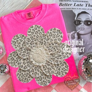 May include: A hot pink sweatshirt with a large flower applique. The flower has leopard print petals and a cream-colored lace center. The words "original designer" are printed on the image.