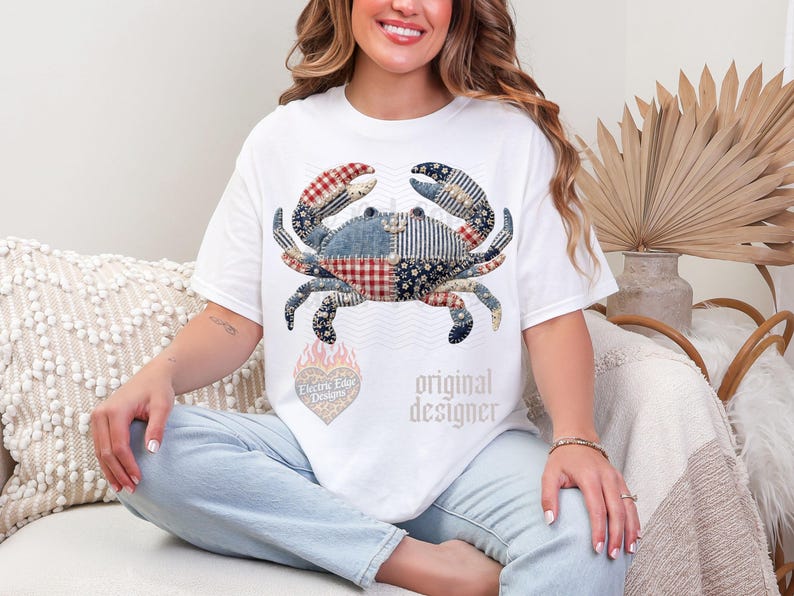 May include: White t-shirt featuring a patchwork crab design in red, blue, and white patterns. The shirt includes the text "original designer" and a heart-shaped logo with text.