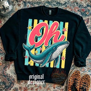 May include: Black sweatshirt with a colorful graphic featuring the word "Oh" in red and a blue whale. The design includes yellow and blue stripes, stars, and the text "original designer" and "Electric Edge Designs".