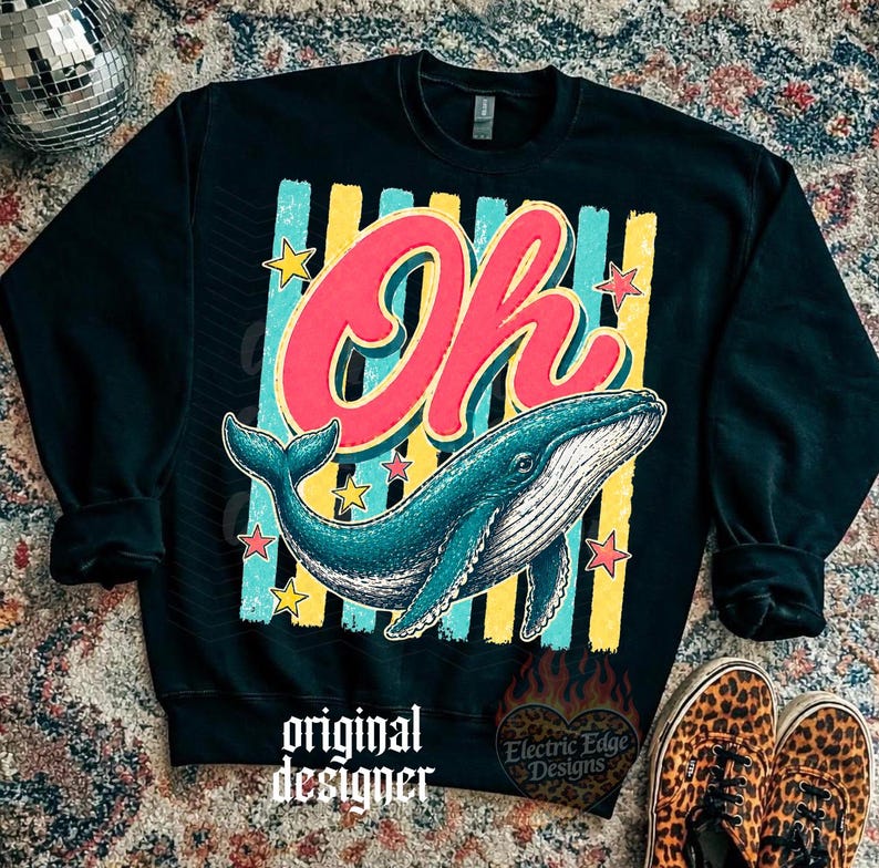 May include: Black sweatshirt with a colorful graphic featuring the word "Oh" in red and a blue whale. The design includes yellow and blue stripes, stars, and the text "original designer" and "Electric Edge Designs".