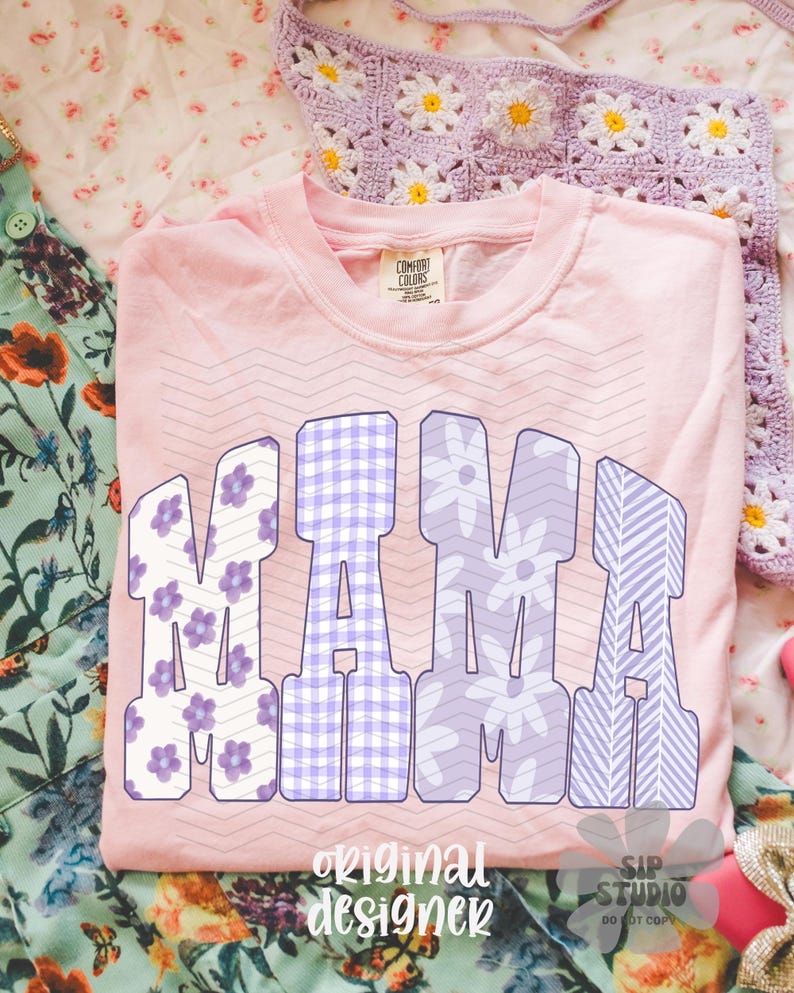 May include: A light pink Comfort Colors t-shirt with the word "MAMA" in large, block letters. The letters feature floral, gingham, and striped patterns in shades of purple and white. The shirt is on a floral patterned surface.