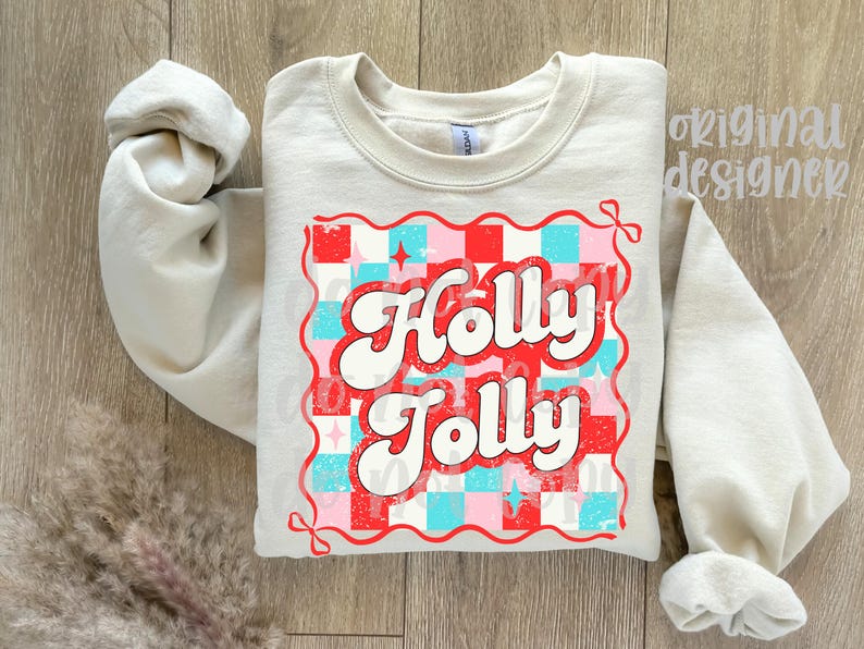 May include: A light beige sweatshirt with the words "Holly Jolly" in a retro font. The text is set against a red, pink, and blue checkered pattern, with a red border. The sleeves are rolled up.