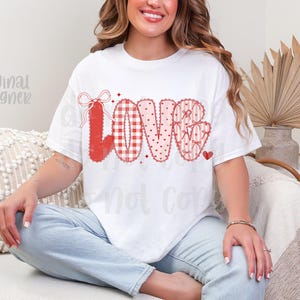May include: White t-shirt with the word "LOVE" in red, featuring various patterns like gingham, hearts, and bows. The shirt has a casual fit and is suitable for Valentine's Day or expressing affection.