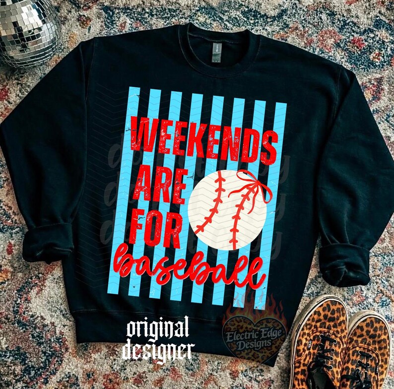 May include: Black sweatshirt featuring the text "Weekends Are For Baseball" in red, with a baseball graphic. The text is set against a light blue striped background. The sweatshirt also has the text "original designer" and a logo.