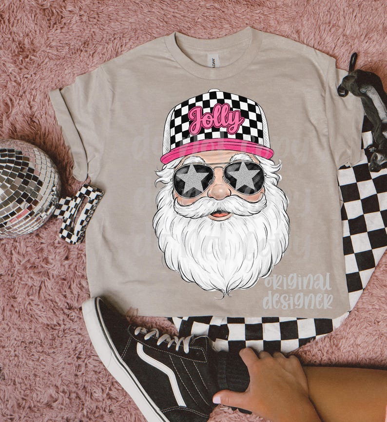 May include: A beige t-shirt featuring a graphic of Santa Claus wearing star-shaped sunglasses and a checkered hat with the word "Jolly". The design includes a long white beard and a pink brim on the hat. The text "original designer" is also visible.