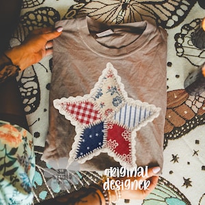 May include: A brown t-shirt with a large, patchwork star applique. The star features red, white, and blue patterned fabrics, including gingham and stripes. The text "original designer" is visible. The shirt is folded on a patterned surface.
