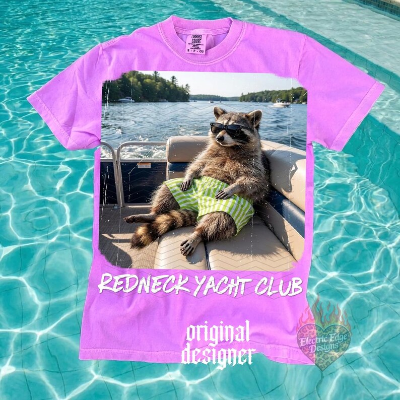 May include: A lilac-colored t-shirt featuring a raccoon wearing sunglasses and green and white striped shorts, lounging on a boat. The shirt has the text "REDNECK YACHT CLUB" and "original designer". A small logo is in the bottom right corner.