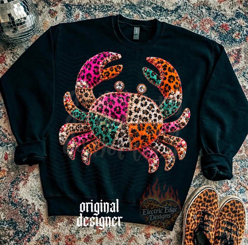 May include: Black sweatshirt featuring a colorful crab design. The crab is made up of patches of leopard print in pink, orange, green, and brown. The words "original designer" are printed on the bottom of the sweatshirt.