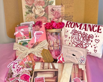 May include: A gift box filled with romantic-themed items. Includes a pillow with "ROMANCE" text, a jar with books, stickers, a rose eye mask, and vintage rose prints. The box is lined with pink tissue paper.