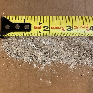 May include: A yellow measuring tape with black markings and a red label that says "25ft" is placed on a brown surface. The tape reads "1 ft 2 STANLEY 3 Life Guard 4".