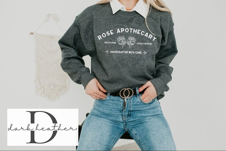 K&ouml;nnte beinhalten: Ein dunkelgrauer Sweatshirt mit dem Text "ROSE APOTHECARY" in Wei&szlig;, mit einem floralen Design und den Worten "ONE OF A KIND", "LOCALLY SOURCED" und "HANDCRAFTED WITH CARE".