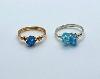 May include: Two wire-wrapped rings with blue crystal stones. The ring on the left has a gold wire and one stone. The ring on the right has a silver wire and two stones.