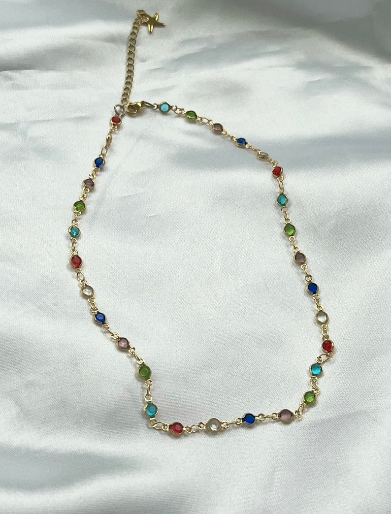 Puede incluir: Un collar de cadena dorada con cuentas redondas de colores. Las cuentas est&aacute;n en un patr&oacute;n de arco&iacute;ris.