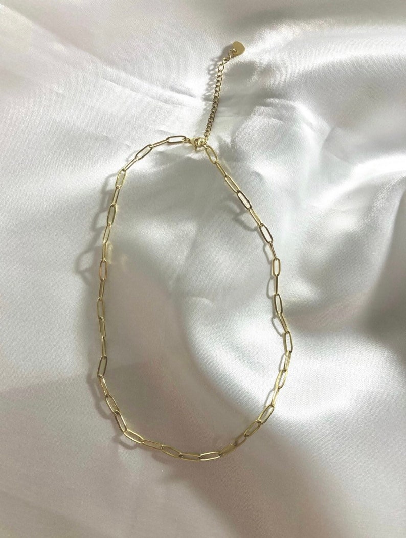 Puede incluir: Un collar de cadena dorada con un cierre en forma de coraz&oacute;n. La cadena est&aacute; hecha de peque&ntilde;as formas ovaladas enlazadas.