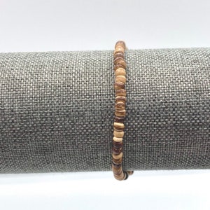 May include: A brown and beige wooden beaded bracelet. The bracelet is made of small, round beads that are strung together on a string.