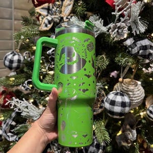 May include: Green stainless steel tumbler with a handle. The tumbler has a design of Jack Skellington from The Nightmare Before Christmas. The text on the tumbler reads "On the Moon at Night".