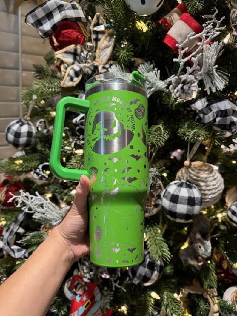 May include: Green stainless steel tumbler with a handle. The tumbler has a design of Jack Skellington from The Nightmare Before Christmas. The text on the tumbler reads "On the Moon at Night".