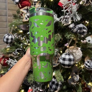May include: A green stainless steel tumbler with a silver design of bats and ghosts. The tumbler has a lid with a straw hole.