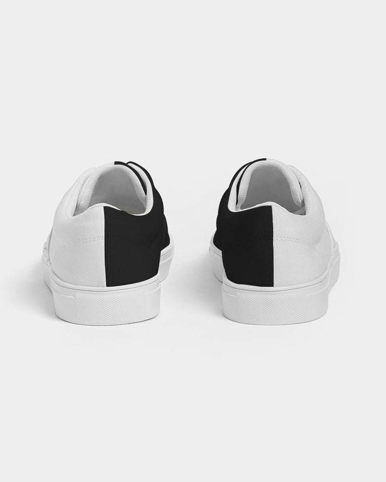 May include: A pair of white canvas low-top trainers with black fabric panels on the sides.