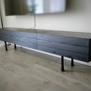 May include: A dark grey wooden media console with four drawers and black metal legs. The console is sitting on a light wood floor.