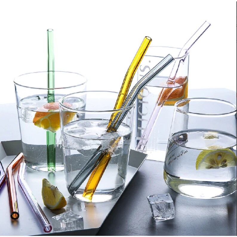 May include: Four clear glass tumblers filled with water and lemon slices. Each tumbler has a different coloured glass straw. The straws are green, yellow, pink and purple.