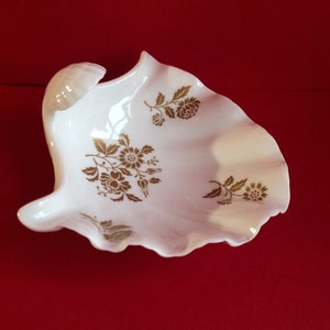 May include: A white porcelain shell-shaped dish with a gold floral design. The dish is perfect for holding small items like jewelry or trinkets.