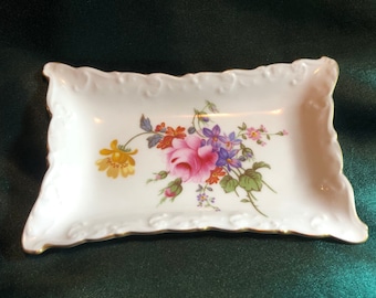 May include: A white porcelain trinket dish with a gold rim and a floral design featuring pink, yellow, purple, and green flowers.