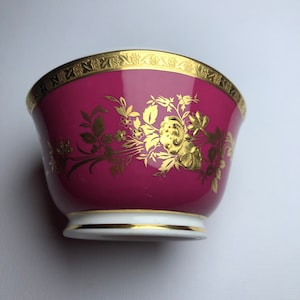 May include: A pink porcelain sugar bowl with a gold floral design and a gold rim.
