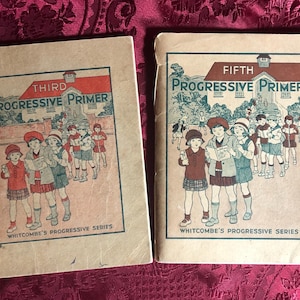 May include: Two antique "Progressive Primer" books. The covers display illustrations of children in school uniforms, with the words "Third" and "Fifth" above the title. The books are part of the "Whitcombe's Progressive Series."