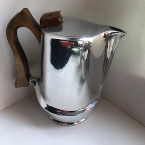 Peut inclure: Une cafetière en argent avec une poignée en bois et un couvercle. La cafetière a un design élégant et moderne.