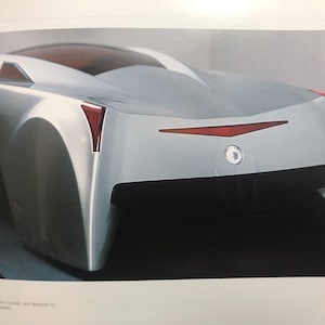 May include: A silver sports car with a red taillight and a Cadillac emblem on the back.