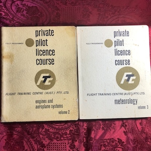 May include: Two vintage books titled "private pilot licence course" with the text "FULLY PROGRAMMED" on the cover. The book on the left is volume 2 and covers engines and aeroplane systems. The book on the right is volume 3 and covers meteorology.