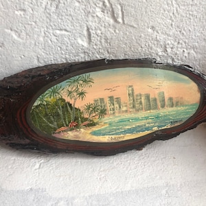 May include: A painted wooden oval with a cityscape and palm trees on a beach. The painting is signed "Sur Streets".