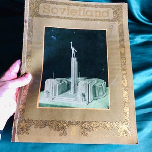 Peut inclure: Couverture de magazine vintage "Sovietland" avec une illustration stylisée d'un monument avec une figure tenant une étoile. La couverture est de ton sépia avec des bordures décoratives dorées et le titre "Sovietland" en haut.