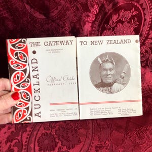 以下が含まれることがあります： 2つのヴィンテージ旅行ガイド。左側のガイドは「The Gateway to Auckland」と題され、赤と黒のマオリ風のデザインが施されています。右側のガイドは「To New Zealand」と題され、セピア色の肖像画が描かれています。どちらのガイドも1938年2月発行です。