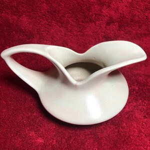 May include: A white ceramic jug with a distinctive, curved design and a wide, open spout. The jug has a smooth, glossy finish.