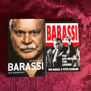 May include: Two hardcover books with black covers and white text. The book on the left is titled "Barassi: The Biography" by Peter Lalor. The book on the right is titled "Barassi: The Life Behind The Legend" by Ron Barassi & Peter McFarline.