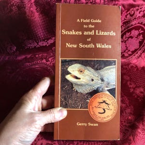 May include: A brown field guide titled "A Field Guide to the Snakes and Lizards of New South Wales." The cover shows a lizard with its mouth open. The book has a circular sticker from the Royal Zoological Society of NSW.