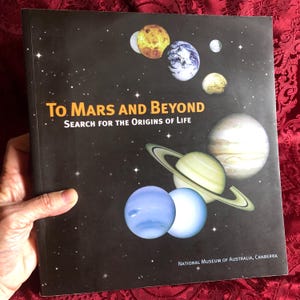 May include: A book titled "To Mars and Beyond" with a dark background featuring illustrations of planets. The cover includes the text "Search for the Origins of Life" and the National Museum of Australia, Canberra logo.