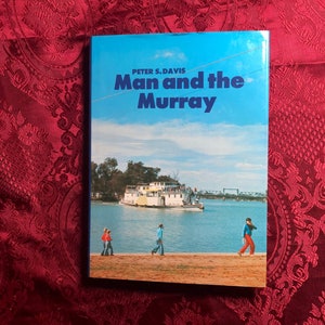 May include: A blue book titled "Man and the Murray" by Peter S. Davis. The cover shows a photograph of a riverboat on a river with people walking along the bank.