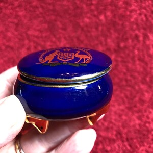 May include: A small, cobalt blue trinket box with gold accents and a lid featuring the Australian coat of arms. The box has three gold feet.