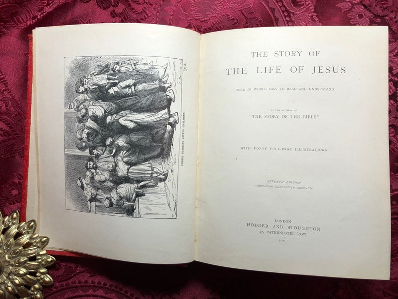 May include: An open book titled "The Story of the Life of Jesus" with a black and white illustration of a group of people. The book is written by the author of "The Story of the Bible" and includes forty full-page illustrations.