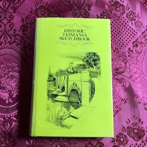 May include: A green book with the title "Historic Tasmania Sketchbook" on the cover. The cover features a black and white illustration of a bridge over a river.